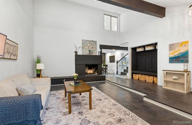 living room featuring hardwood / wood-style flooring, beamed ceiling, a high ceiling, and a brick fireplace