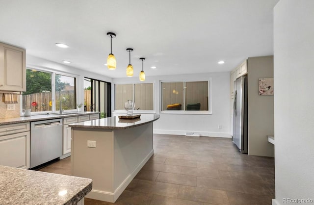 kitchen featuring hanging light fixtures, light stone countertops, stainless steel appliances, sink, and a center island