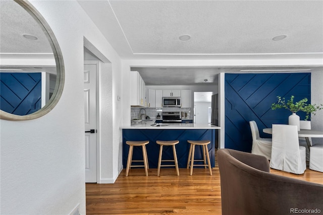 kitchen with wood finished floors, a breakfast bar, decorative backsplash, appliances with stainless steel finishes, and white cabinetry