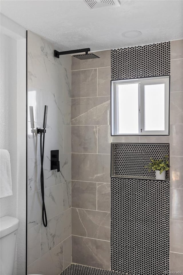 full bath featuring tiled shower, toilet, and visible vents