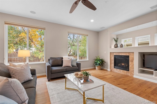 living room with a tile fireplace, light hardwood / wood-style floors, and ceiling fan