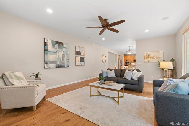 living room featuring light hardwood / wood-style flooring and ceiling fan with notable chandelier