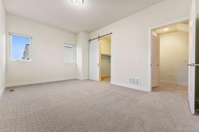 unfurnished bedroom with light carpet, a barn door, visible vents, and baseboards