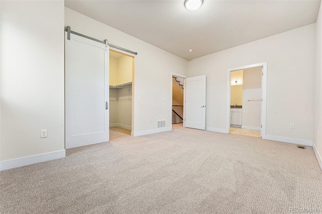 unfurnished bedroom featuring a walk in closet, a closet, a barn door, light carpet, and baseboards