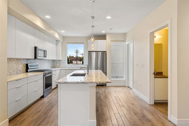 kitchen featuring stainless steel appliances, an island with sink, light wood finished floors, white cabinetry, and decorative backsplash