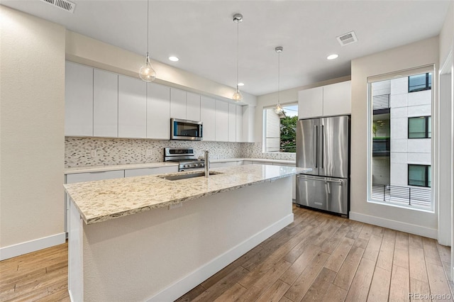 kitchen featuring stainless steel appliances, tasteful backsplash, a center island with sink, light wood finished floors, and baseboards