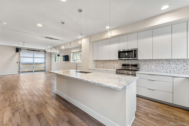 kitchen with stainless steel appliances, a sink, white cabinets, hanging light fixtures, and modern cabinets