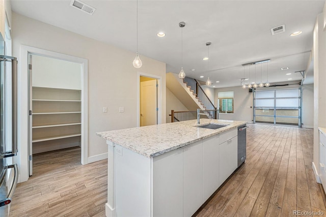 kitchen with a sink, visible vents, white cabinetry, a center island with sink, and pendant lighting