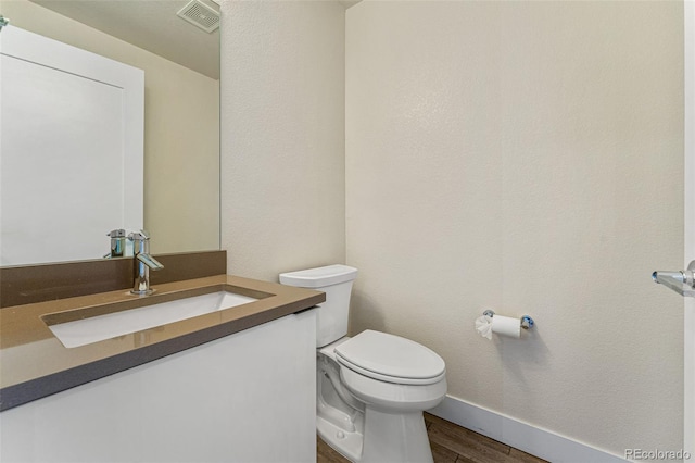 half bath featuring baseboards, visible vents, toilet, wood finished floors, and vanity