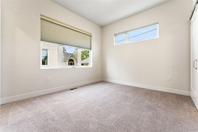 empty room with carpet, visible vents, and baseboards