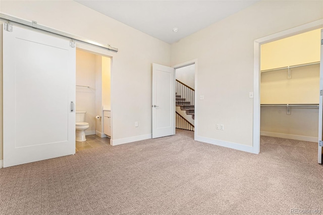 unfurnished bedroom featuring a closet, a spacious closet, a barn door, light carpet, and baseboards