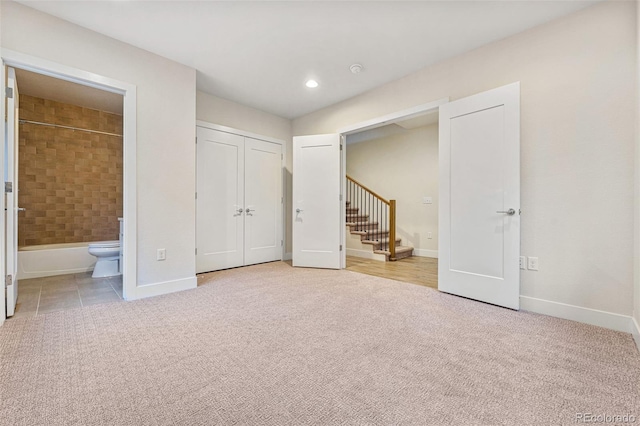 unfurnished bedroom with recessed lighting, light colored carpet, baseboards, a closet, and ensuite bath