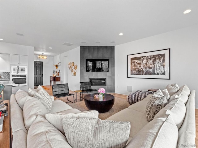 living room featuring a large fireplace, light wood-style floors, baseboards, and recessed lighting