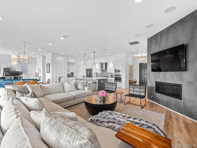 living room featuring light wood-type flooring, a large fireplace, visible vents, and recessed lighting