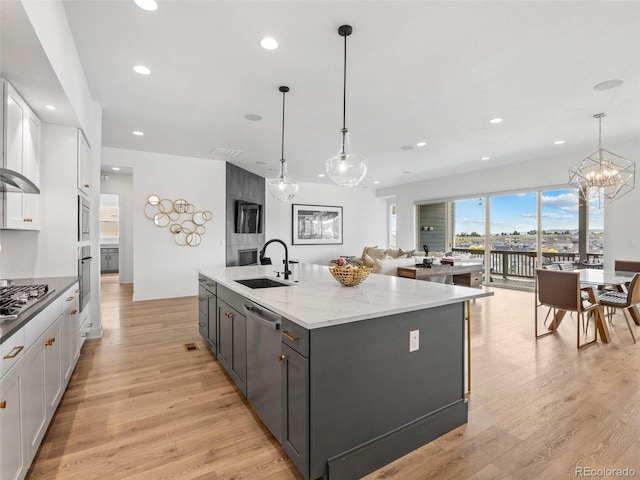 kitchen featuring stainless steel appliances, hanging light fixtures, a center island with sink, and sink