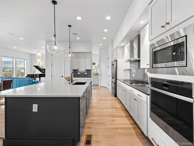 kitchen featuring visible vents, a spacious island, wall chimney exhaust hood, appliances with stainless steel finishes, and a sink