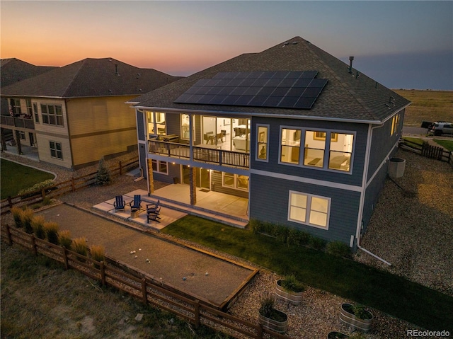 back house at dusk featuring solar panels, a balcony, and a patio area