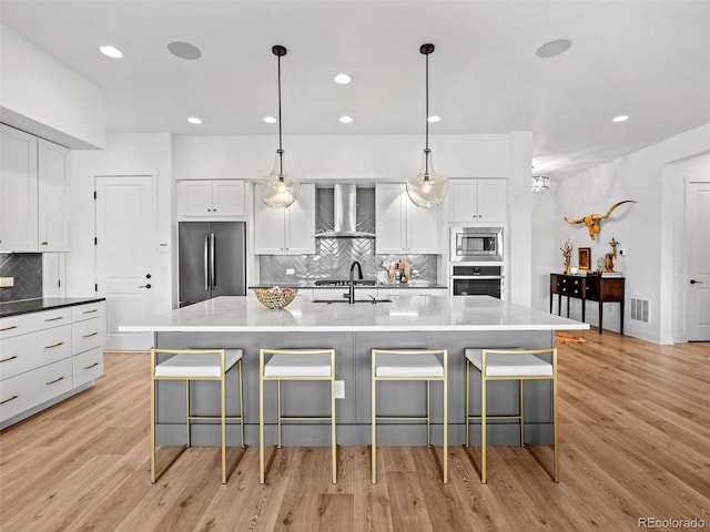 kitchen featuring visible vents, appliances with stainless steel finishes, white cabinetry, wall chimney range hood, and light wood-type flooring