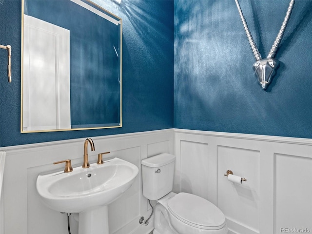 half bath featuring a textured wall, wainscoting, a sink, and toilet