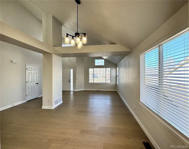 spare room with visible vents, a notable chandelier, high vaulted ceiling, wood finished floors, and baseboards