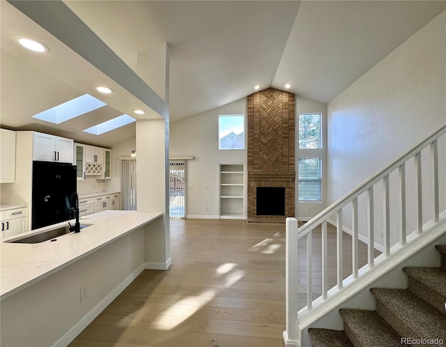 kitchen with a sink, black refrigerator, wood finished floors, white cabinetry, and glass insert cabinets