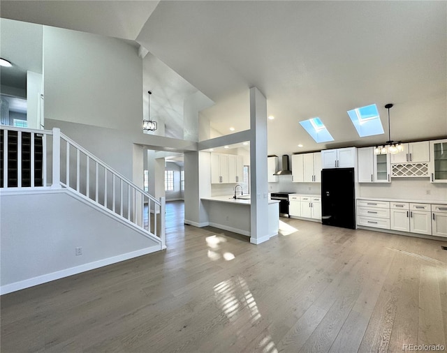 unfurnished living room featuring baseboards, stairway, light wood-type flooring, a skylight, and a sink