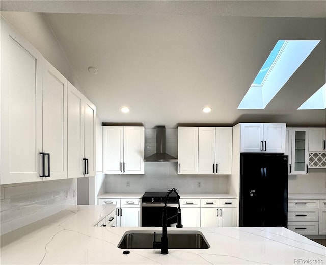 kitchen featuring a sink, range with electric stovetop, freestanding refrigerator, wall chimney range hood, and light stone countertops