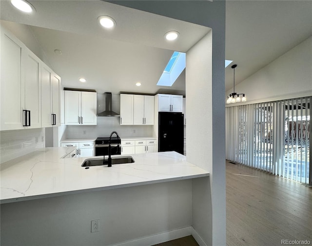 kitchen featuring a peninsula, vaulted ceiling with skylight, stainless steel electric range, a sink, and wall chimney exhaust hood