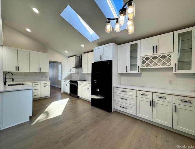 kitchen with freestanding refrigerator, a sink, electric stove, lofted ceiling with skylight, and wall chimney exhaust hood