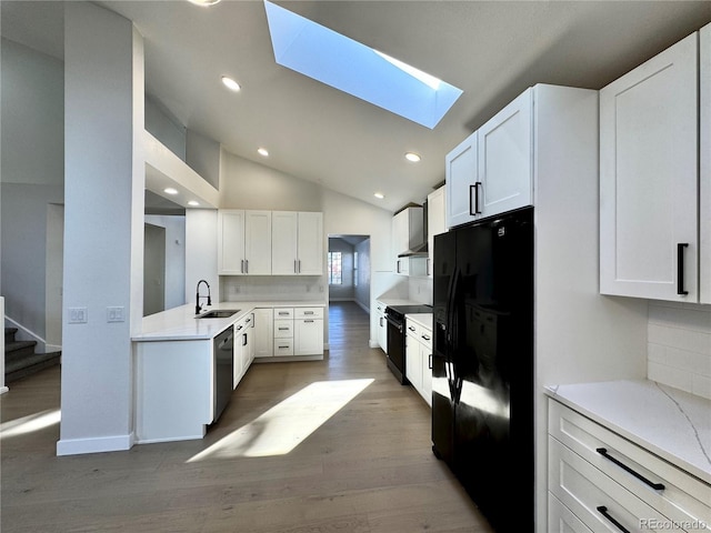 kitchen featuring lofted ceiling with skylight, white cabinetry, black appliances, and a sink