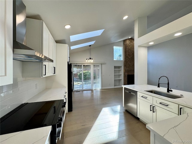 kitchen with wall chimney range hood, light stone countertops, a skylight, stainless steel dishwasher, and a sink