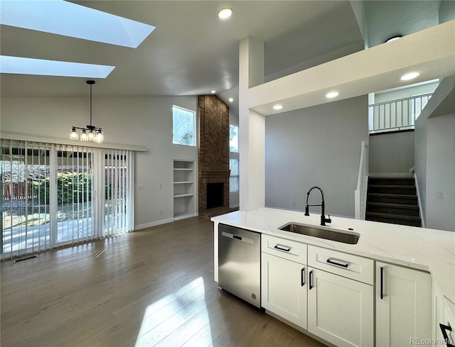 kitchen with a sink, a brick fireplace, light stone counters, wood finished floors, and stainless steel dishwasher