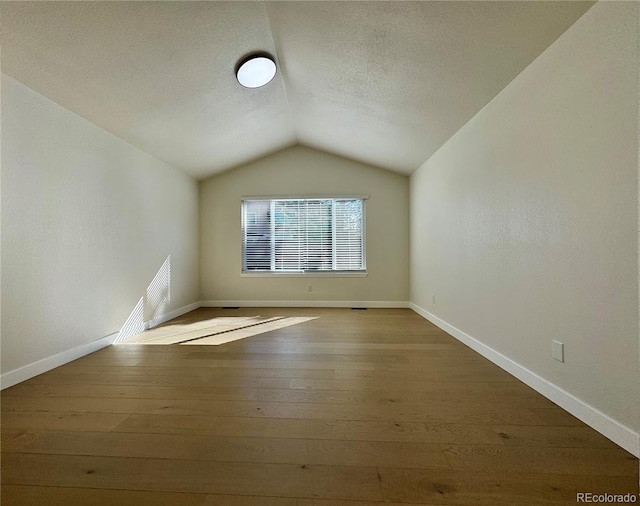 unfurnished room featuring hardwood / wood-style floors, lofted ceiling, baseboards, and a textured ceiling