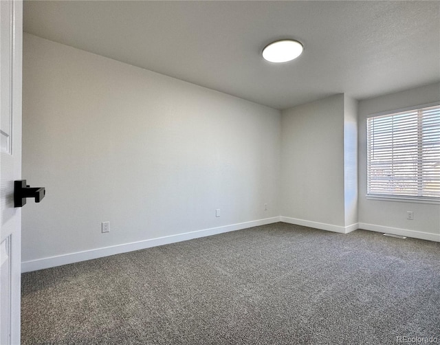 unfurnished room with baseboards and dark carpet