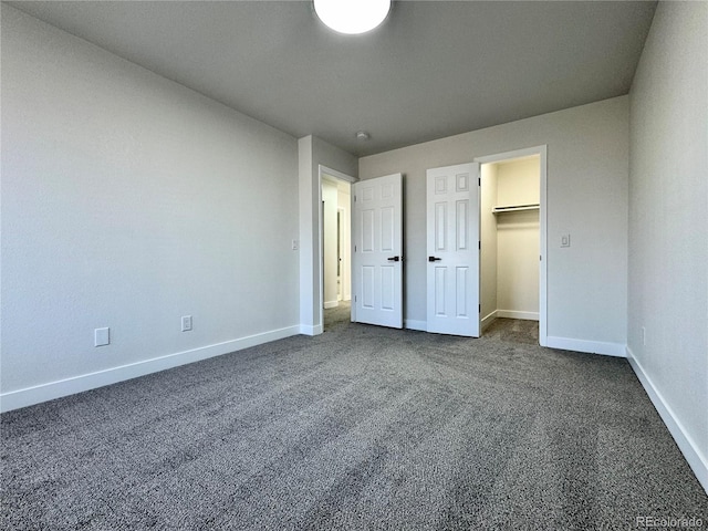 unfurnished bedroom featuring a spacious closet, baseboards, and dark colored carpet