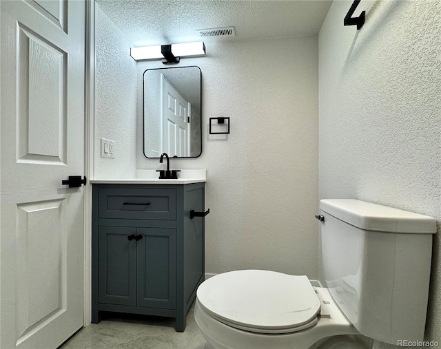 half bath with visible vents, toilet, vanity, and a textured wall