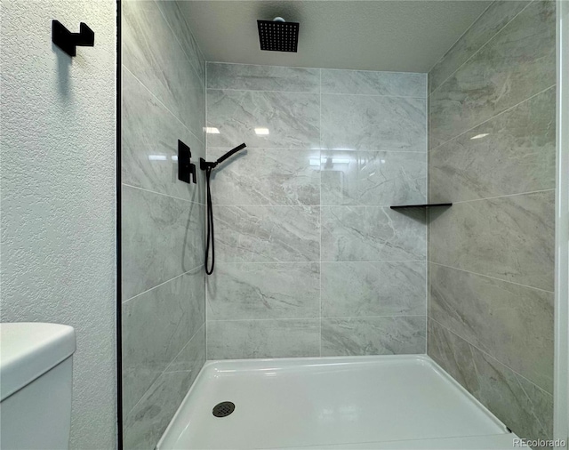 bathroom featuring tiled shower, toilet, and a textured wall