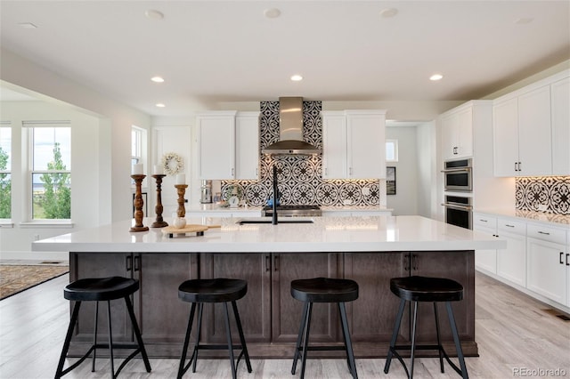 kitchen with a large island, wall chimney exhaust hood, white cabinets, and a breakfast bar area