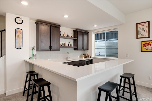 kitchen with kitchen peninsula, light carpet, a breakfast bar, dark brown cabinets, and sink