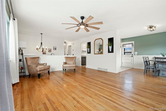 living area with ceiling fan with notable chandelier and light wood-type flooring