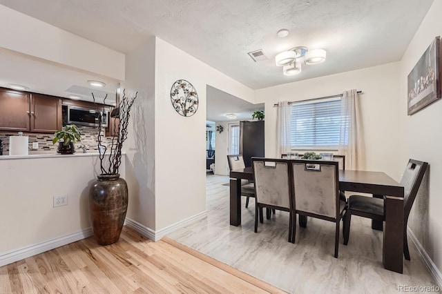 dining area with a textured ceiling and light hardwood / wood-style flooring