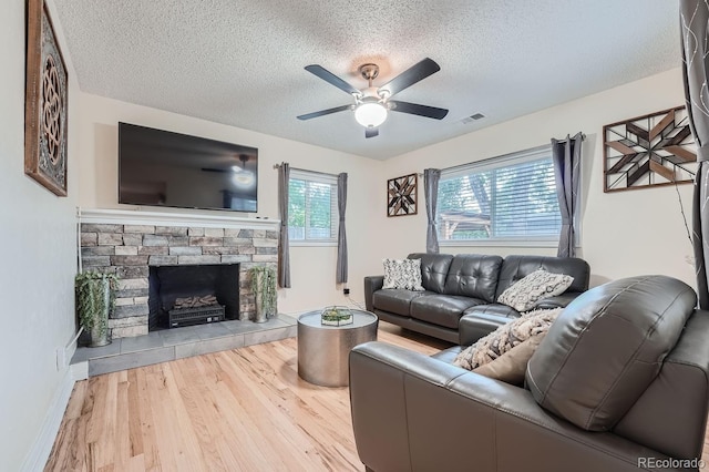 living room featuring wood-type flooring, a textured ceiling, ceiling fan, and a fireplace