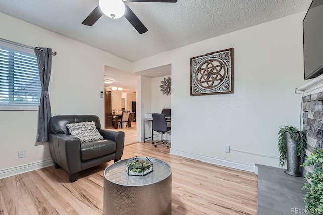 living room featuring ceiling fan, light hardwood / wood-style floors, and a textured ceiling