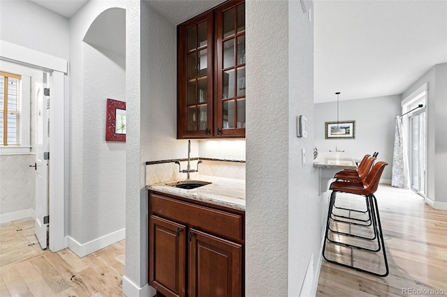 8276 E 28th Dr, Denver, CO 80238 - indoor wet bar with light wood-style flooring, a textured wall, baseboards, and decorative backsplash