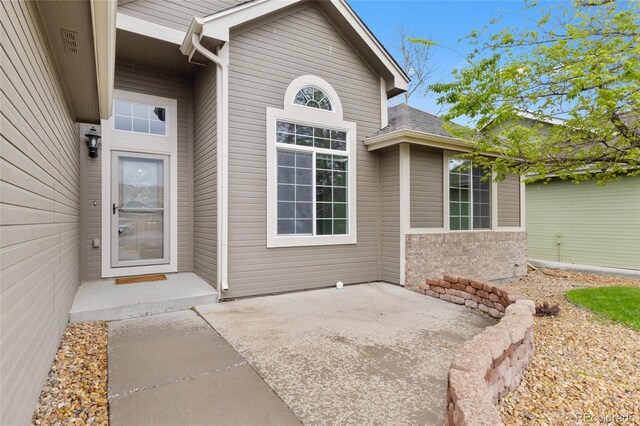 view of exterior entry featuring a patio area and roof with shingles