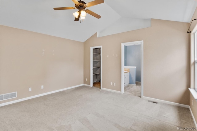 unfurnished bedroom featuring light colored carpet, vaulted ceiling, a spacious closet, baseboards, and connected bathroom