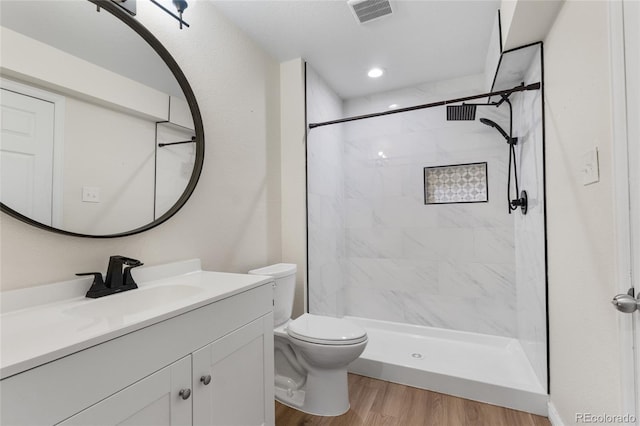 full bath featuring wood finished floors, vanity, toilet, and a tile shower