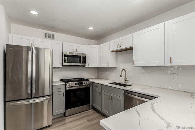 1000 Worchester St, Aurora, CO 80011 - kitchen featuring appliances with stainless steel finishes, gray cabinets, decorative backsplash, light wood-style flooring, and light stone countertops