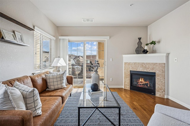 living area with a tiled fireplace, wood finished floors, visible vents, and baseboards