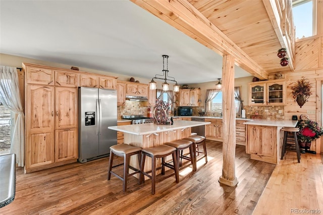 kitchen with a kitchen bar, stainless steel appliances, decorative light fixtures, light hardwood / wood-style flooring, and a center island